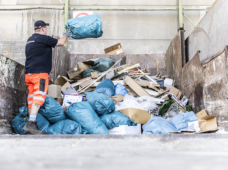 Ein Mann wirft einen Abfallsack auf einen Müllhaufen