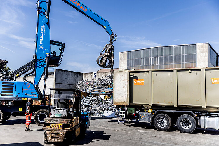 Ein Kran belädt einen LKW mit Container auf einem Schrottplatz