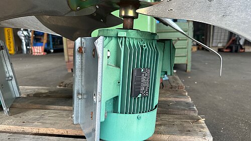 Industrieventilator mit Elektromotor Grüner Elektromotor auf einer Palette, montiert unter einem großen Industrieventilator, in einer Werkhalle.